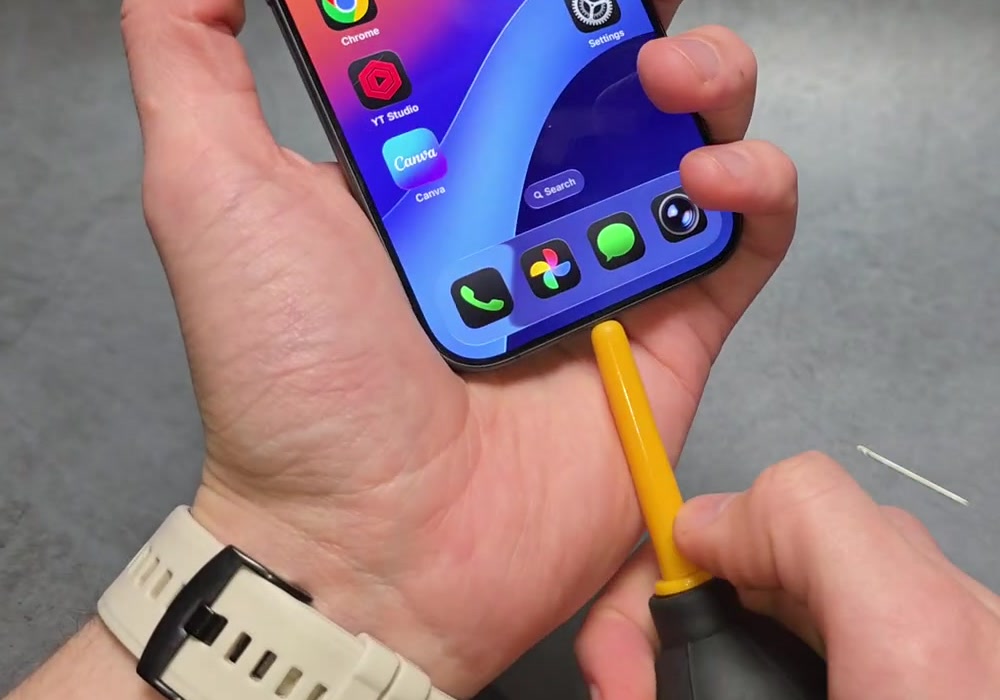 A yellow bulb blower nozzle held at the bottom edge of an iPhone next to the charging port