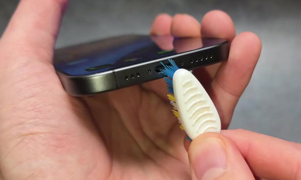 Soft brush bristles being worked into the charging port of an iPhone held on its side