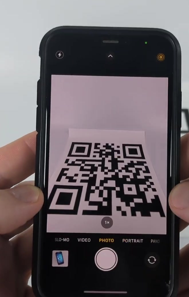 iPhone Camera app in Photo mode framing a printed QR code in the viewfinder