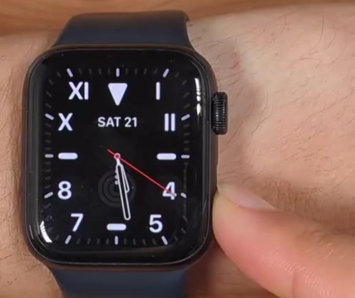 A finger pressing and holding the side button on an Apple Watch while the watch face is still showing
