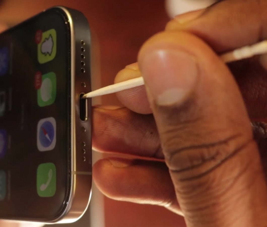 A wooden toothpick being used to lift debris from an iPhone charging port