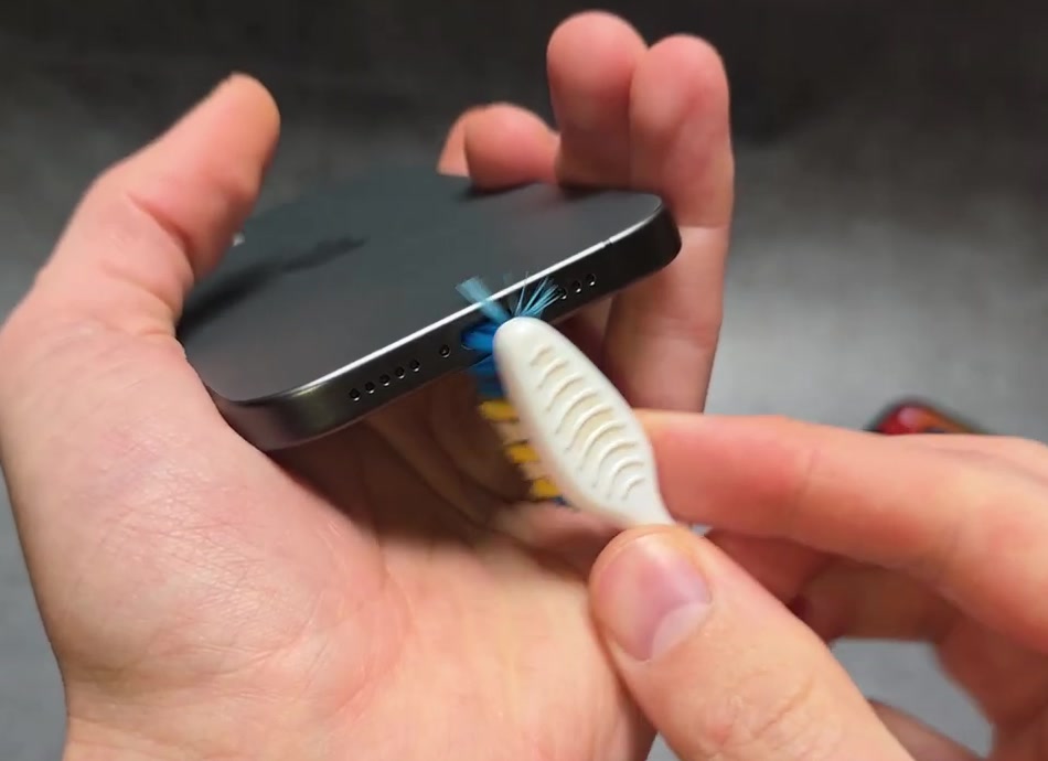 A small soft-bristled brush being used to clean an iPhone charging port