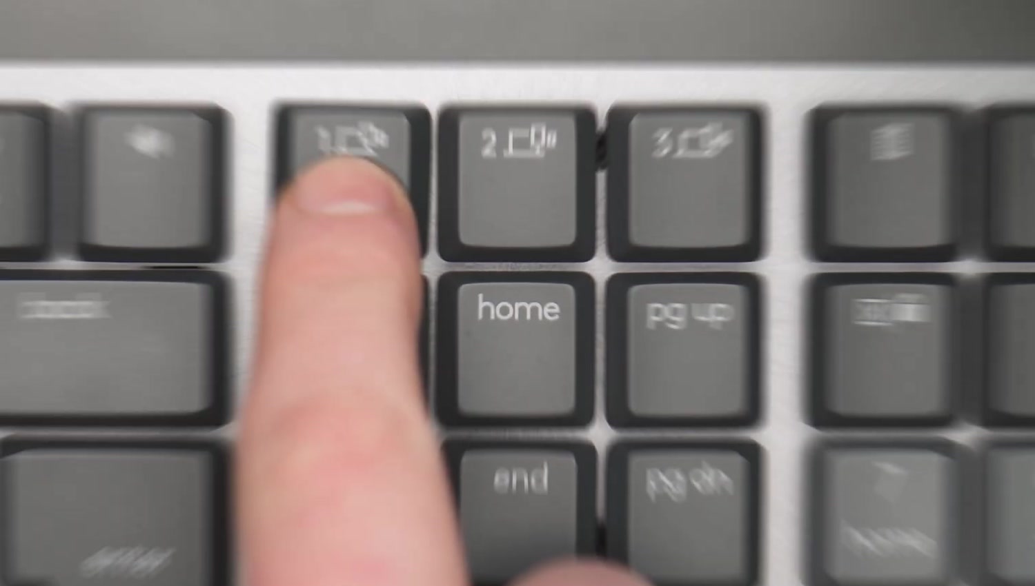 Close-up of a finger pressing the Easy-Switch key marked 1 on the top row of a Logitech keyboard