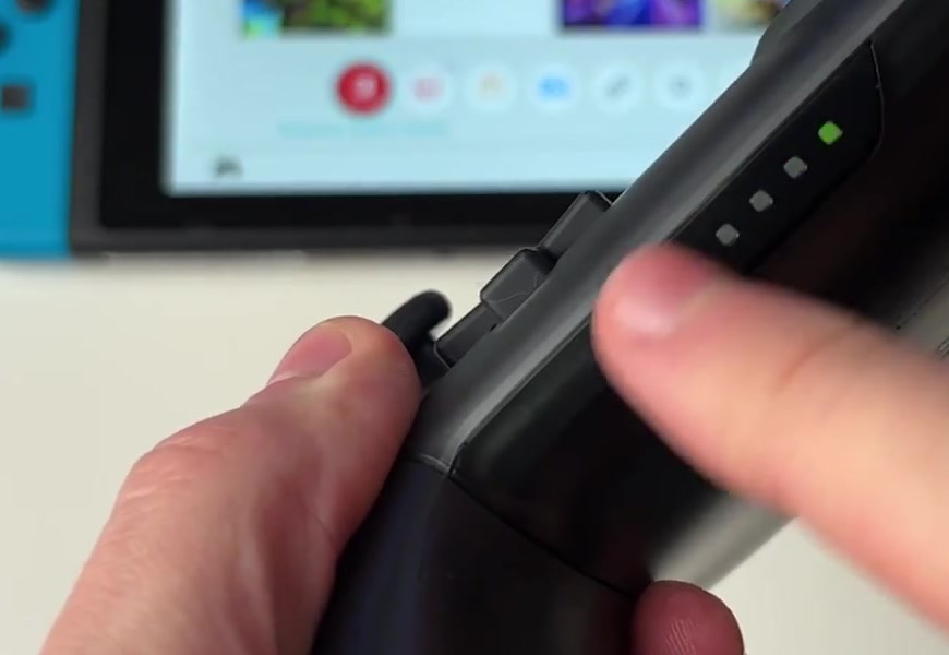 A finger pressing the SYNC button on the top edge of a Switch Pro Controller with the player indicator lights visible
